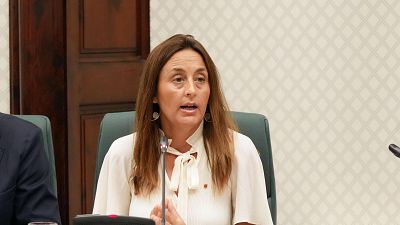Esther Niubó, Consellera d'Educació, compareix al Parlament. Té cabell llarg castany, brusa clara amb coll alt i porta un pin. Està asseguda, parlant amb micròfon i fent gest amb la mà. Esther Niubó, Consellera d'Educació, compareix al Parlament. Té cabell llarg castany, brusa clara amb coll alt i porta un pin. Està asseguda, parlant amb micròfon i fent gest amb la mà.
