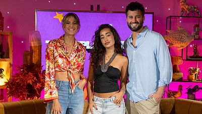 Lorena Castell, Lola Índigo y Pablo González Batista sonríen en un plató de "Teleplanistas" con iluminación morada y fucsia. Se aprecian detalles de sus atuendos y elementos decorativos. Lorena Castell, Lola Índigo y Pablo González Batista sonríen en un plató de "Teleplanistas" con iluminación morada y fucsia. Se aprecian detalles de sus atuendos y elementos decorativos.
