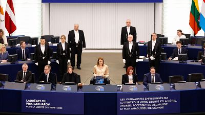 Roberta Metsola preside una ceremonia en el Parlamento Europeo, con un micrófono frente a ella. Se observa a personas vestidas formalmente y banderas en el fondo, con textos sobre el Premio Sájarov. Roberta Metsola preside una ceremonia en el Parlamento Europeo, con un micrófono frente a ella. Se observa a personas vestidas formalmente y banderas en el fondo, con textos sobre el Premio Sájarov.