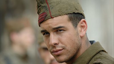 Mario Casas caracterizado como personaje de 'La mula', con uniforme militar verde oliva, gorra y expresión seria. Fondo desenfocado.