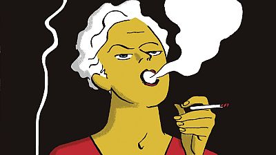 En un primer plano de un cómic, una mujer con piel amarilla y cabello blanco fuma, mostrando una expresión de desaprobación. Viste una blusa roja y sostiene otro cigarrillo encendido, con humo saliendo de su boca.