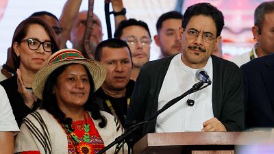 Iván Cépeda y Aida Quilcué en un evento público. Cépeda con gafas y barba, Quilcué con sombrero y poncho. Fondo con público. Iván Cépeda y Aida Quilcué en un evento público. Cépeda con gafas y barba, Quilcué con sombrero y poncho. Fondo con público.
