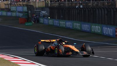 Coche de F1 naranja y negro #81 con patrocinador 'aVerMedia', tomando una curva en una pista con gradas y publicidad al fondo. Coche de F1 naranja y negro #81 con patrocinador 'aVerMedia', tomando una curva en una pista con gradas y publicidad al fondo.