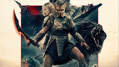 Un Predator con armadura y espada roja se enfrenta a diversas criaturas y humanos en un cartel de película, con un fondo que sugiere un entorno desértico y postapocalíptico. Un Predator con armadura y espada roja se enfrenta a diversas criaturas y humanos en un cartel de película, con un fondo que sugiere un entorno desértico y postapocalíptico.