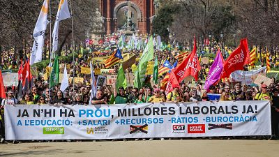 Manifestación de docentes en Barcelona por mejoras laborales y educativas, con pancarta principal "JA N'HI HA PROU, MILLORES LABORALS JA! A L'EDUCACIÓ: +SALARI +RECURSOS -RÀTIOS -BUROCRÀCIA" y logos sindicales. Fondo: Arc de Triomf.