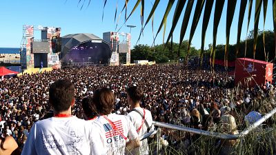 Festival de música al aire libre con miles de asistentes, un gran escenario con el texto "LA FESTA DEL SEGLE MIL" y un cubo rojo de "ESTRELLA" en el lateral.