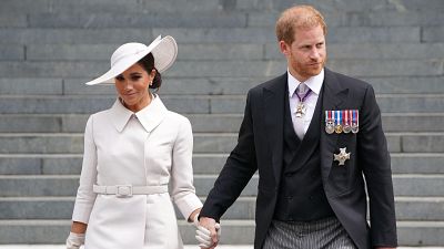 Príncipe Harry y Meghan Markle, Duques de Sussex, tomados de la mano, posan ante una imponente escalera de piedra. Ella viste de blanco roto, él de chaqué oscuro con condecoraciones. Príncipe Harry y Meghan Markle, Duques de Sussex, tomados de la mano, posan ante una imponente escalera de piedra. Ella viste de blanco roto, él de chaqué oscuro con condecoraciones.