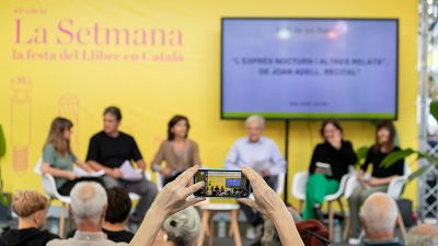 Panell de discussió a la 41a edició de "La Setmana, la festa del Llibre en Català", amb cinc ponents i una pantalla que mostra "L'EXPRESSIÓ NOCTURNA I L'ALTRE RELAT". Panell de discussió a la 41a edició de "La Setmana, la festa del Llibre en Català", amb cinc ponents i una pantalla que mostra "L'EXPRESSIÓ NOCTURNA I L'ALTRE RELAT".