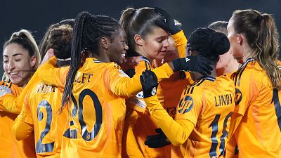 Celebración de jugadoras del Real Madrid tras un gol o victoria en partido de la UEFA Women's Champions League. Se ven dorsales 2, 18 (LINDA) y 20 (OLLET) en camisetas naranjas.