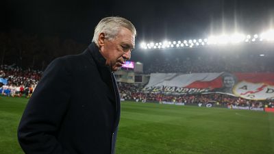 Imagen de Carlo Ancelotti al borde del campo, con la cabeza baja. Aficionados en la grada y la iluminación del estadio son visibles. Contexto: tensión entre optimismo y expectativas. Imagen de Carlo Ancelotti al borde del campo, con la cabeza baja. Aficionados en la grada y la iluminación del estadio son visibles. Contexto: tensión entre optimismo y expectativas.