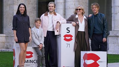 Cinco miembros del equipo de una producción cinematográfica posan sonrientes sobre el césped junto a tótems publicitarios blancos.