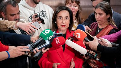 La Ministra de Defensa, Margarita Robles, atiende a los medios de comunicación, rodeada de micrófonos con logotipos de varios medios, con una chaqueta roja y una expresión seria. La Ministra de Defensa, Margarita Robles, atiende a los medios de comunicación, rodeada de micrófonos con logotipos de varios medios, con una chaqueta roja y una expresión seria.