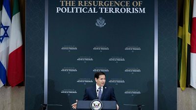 Marco Rubio habla en un evento con el titular "THE RESURGENCE OF POLITICAL TERRORISM" y el Gran Sello de EE.UU. de fondo. Banderas de Israel, Italia, Jamaica y Canadá flanquean la escena. Marco Rubio habla en un evento con el titular "THE RESURGENCE OF POLITICAL TERRORISM" y el Gran Sello de EE.UU. de fondo. Banderas de Israel, Italia, Jamaica y Canadá flanquean la escena.