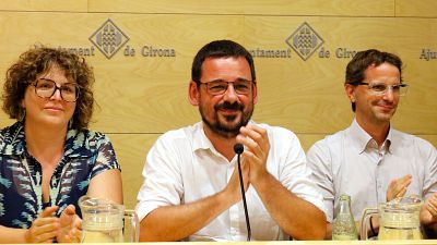 Lluc Salellas, alcalde de Girona, aplaude junto a dos personas en un evento del Ayuntamiento. El fondo muestra el escudo y el nombre de la ciudad. Lluc Salellas, alcalde de Girona, aplaude junto a dos personas en un evento del Ayuntamiento. El fondo muestra el escudo y el nombre de la ciudad.