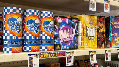 Estant de botiga amb focs artificials: cilindres "LA FONT COI", caixes "TRIANGULO DE CRACKER", "FUENTE DE ORO", "FONT BRUIXA del N...", "FONT del ANTONI" i cartell "NO DEIXIS PASSAR AQUESTA OFERTA DE 4X3!". Estant de botiga amb focs artificials: cilindres "LA FONT COI", caixes "TRIANGULO DE CRACKER", "FUENTE DE ORO", "FONT BRUIXA del N...", "FONT del ANTONI" i cartell "NO DEIXIS PASSAR AQUESTA OFERTA DE 4X3!".