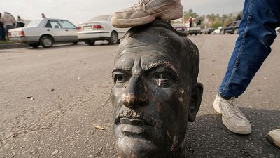 Busto roto en el suelo, pisado por una zapatilla blanca. Fondo con coches aparcados. Posible acto de desafío. Busto roto en el suelo, pisado por una zapatilla blanca. Fondo con coches aparcados. Posible acto de desafío.