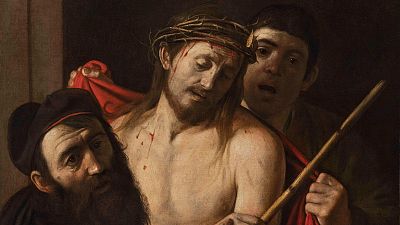 Jesús, con corona de espinas y heridas de sangre, es presentado por un hombre joven con una vara a otro con turbante oscuro. Detalle del 'Ecce Homo' de Caravaggio. Jesús, con corona de espinas y heridas de sangre, es presentado por un hombre joven con una vara a otro con turbante oscuro. Detalle del 'Ecce Homo' de Caravaggio.