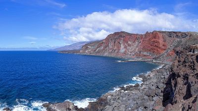 El Mar de las Calmas en El Hierro, con acantilados rocosos, un mar azul y montañas rojizas al fondo