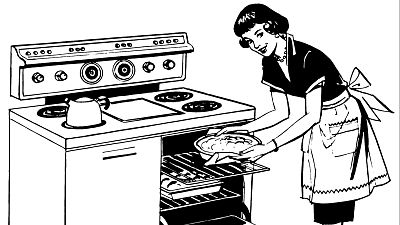 Una mujer sonriente, con el pelo oscuro y peinado con ondas, introduce una tarta en un horno antiguo. La mujer lleva un vestido oscuro con cuello blanco, un collar de perlas y un delantal blanco con un lazo. Una mujer sonriente, con el pelo oscuro y peinado con ondas, introduce una tarta en un horno antiguo. La mujer lleva un vestido oscuro con cuello blanco, un collar de perlas y un delantal blanco con un lazo.