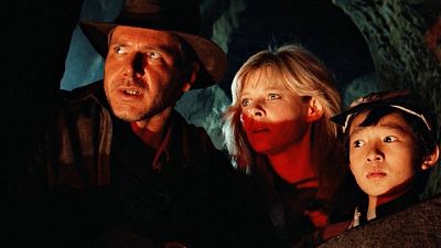 Tres personajes, con expresiones de alerta y miedo, observan algo fuera de cuadro en una cueva oscura con iluminación rojiza.