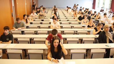 Aula de exámenes con numerosos estudiantes jóvenes concentrados en sus pupitres. Ambiente de seriedad y estudio. Aula de exámenes con numerosos estudiantes jóvenes concentrados en sus pupitres. Ambiente de seriedad y estudio.