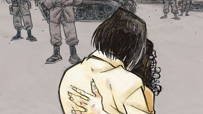 En primer plano, una pareja se abraza; uno de ellos, de espaldas, con cabello oscuro y camisa clara, muestra manos con heridas. Al fondo, se intuyen figuras de soldados y un tanque, evocando un contexto de conflicto. En primer plano, una pareja se abraza; uno de ellos, de espaldas, con cabello oscuro y camisa clara, muestra manos con heridas. Al fondo, se intuyen figuras de soldados y un tanque, evocando un contexto de conflicto.