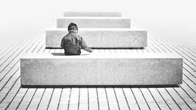 Niño de espaldas en banco, imagen en blanco y negro. Suelo embaldosado, bancos en filas. Título: "Objetivo igualdad". Niño de espaldas en banco, imagen en blanco y negro. Suelo embaldosado, bancos en filas. Título: "Objetivo igualdad".