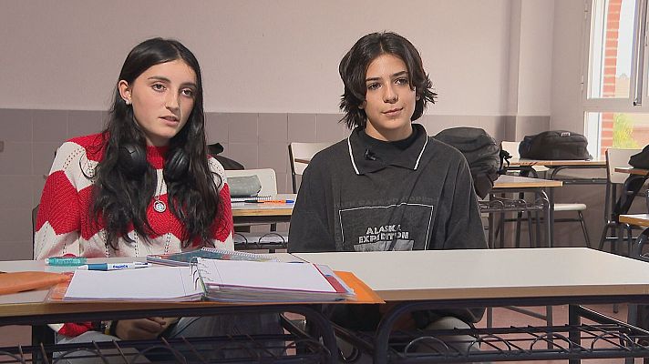 Jóvenes sentados en un aula, posiblemente durante una entrevista para un reportaje. Ella viste un jersey a rayas rojas y blancas, él una sudadera oscura con texto.