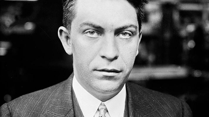 Retrato en blanco y negro de un hombre con traje y corbata, mirando directamente a la cámara. Pelo corto y oscuro; expresión seria.