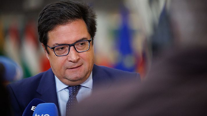 Óscar López, en traje azul marino y gafas, participa en una entrevista o rueda de prensa. Un micrófono de TVE está visible.