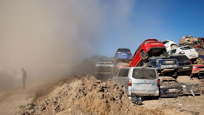 Coches dañados y amontonados en un descampado polvoriento. Una persona se ve entre una nube de polvo.