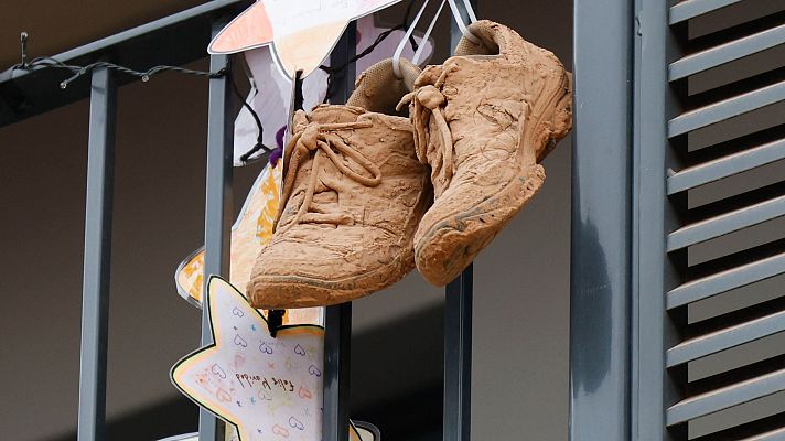 Zapatillas de niño cubiertas de barro, junto a estrellas de papel, cuelgan de un balcón.  Imagen que refleja las consecuencias de una inundación.