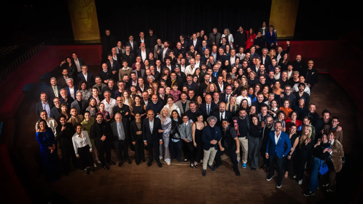 Numerosos nominados a los Premios Goya 2025, vestidos de gala, posan juntos en un teatro antes de la ceremonia.