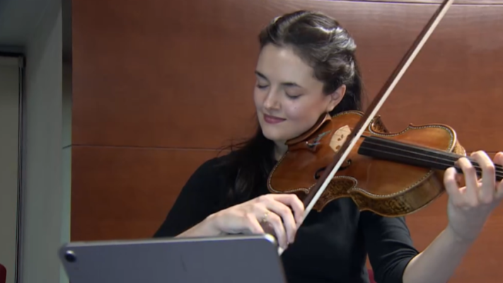 Violista concentrada interpretando una pieza musical desde un atril con partitura, momentos antes de un concierto.
