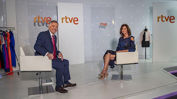 Plató de televisión luminoso con dos personas sentadas en sillas blancas; vestuario y maniquíes presentes. Ambiente moderno y limpio.