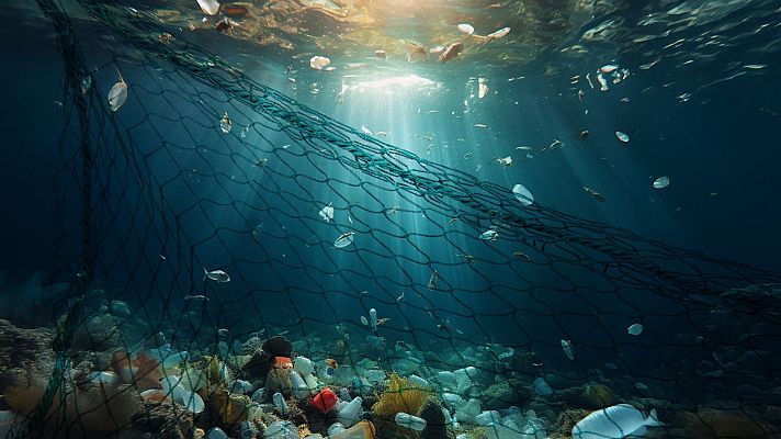 Red de pesca en el mar con peces atrapados y abundante basura en el fondo marino.  Iluminación dramática que resalta la contaminación.