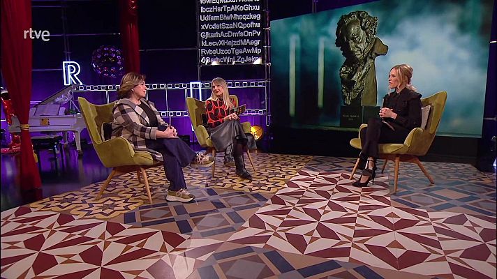 Tres mujeres sentadas en un plató de televisión, con ropa variada, discuten ante una pantalla con un busto y un piano de cola al fondo.