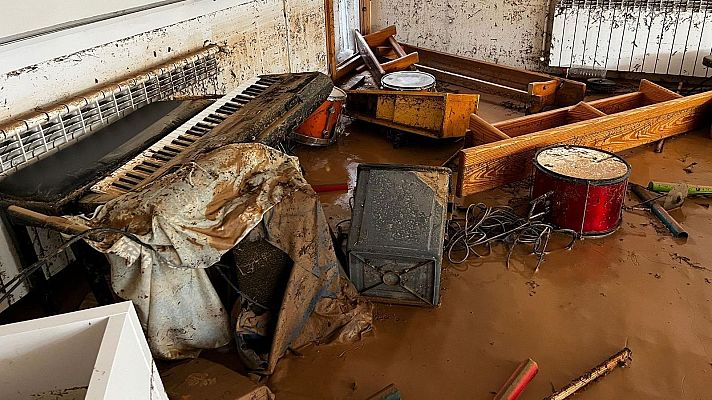 Habitación inundada de barro tras una DANA.  Piano, tambor naranja y amplificador dañados.  Cables y escombros visibles.  Devastación y pérdida material.