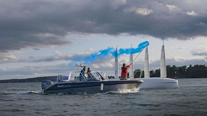Lancha con tres personas y bengala azul navegando junto a un velero de tres mástiles en un entorno acuático con árboles y cielo nublado.