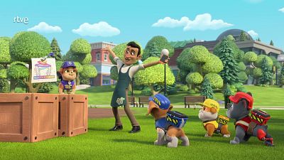 Rubble presenta un dibujo infantil; un adulto celebra con un móvil; otros cachorros observan. Escena en un parque.