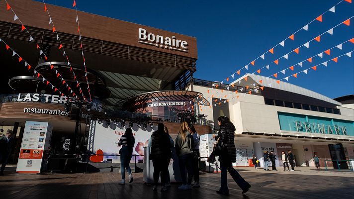 Banderines decoran el centro comercial, mostrando actividad y ambiente festivo con personas caminando frente a tiendas como Primark y un área de restaurantes.