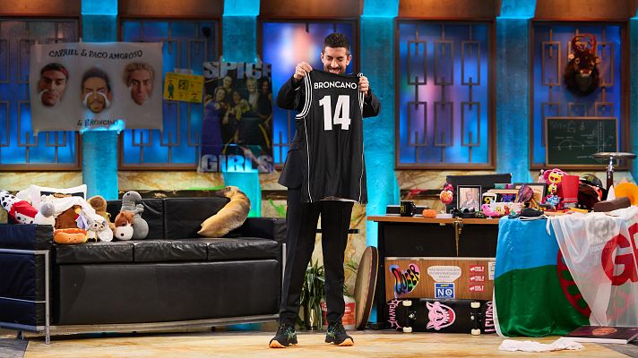 David Broncano presenta una camiseta negra con el número 14 en un plató con sofá, mesa y pósters.