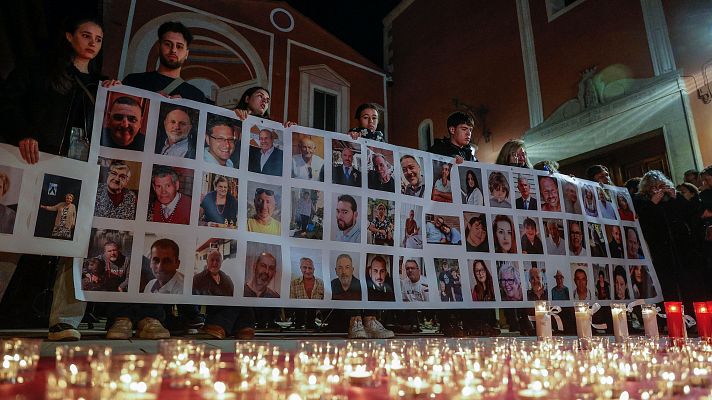 Con velas y pancarta con fotos, un grupo recuerda a las víctimas en un acto nocturno frente a un edificio de estilo eclesiástico.