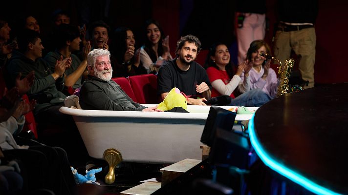 Dos hombres en una bañera sobre un escenario teatral, rodeados de peluches y un saxofón dorado. El público aplaude.