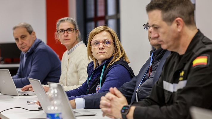 Reunión de trabajo: varias personas, incluyendo a Pilar Bernabé, sentadas alrededor de una mesa con ordenadores portátiles, con expresiones serias.