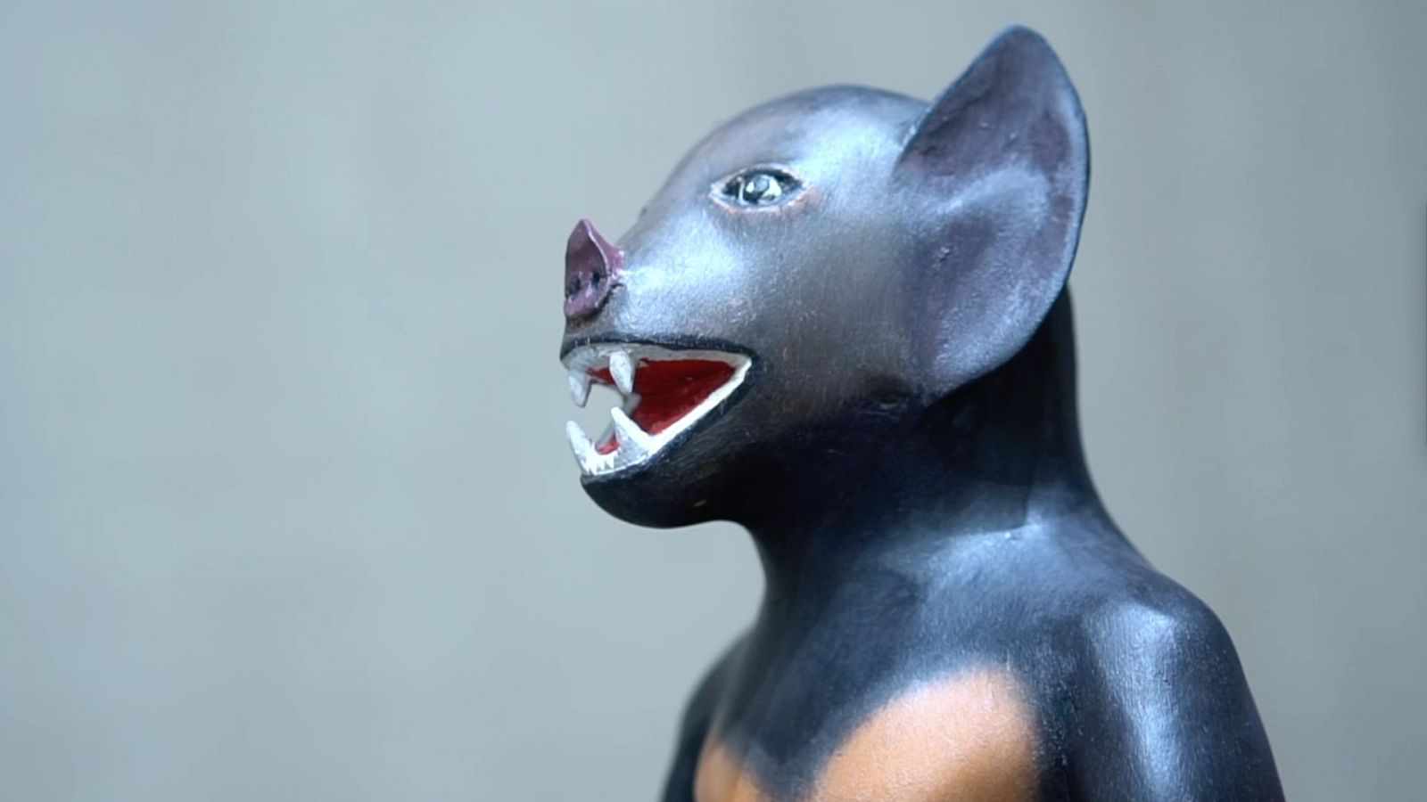 Escultura de murciélago de perfil, con cabeza oscura, dientes blancos y torso más claro.  Detalles realistas en cabeza y orejas.