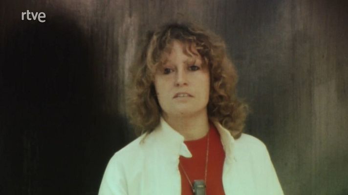 Mujer rubia con camisa blanca y micrófono, en un archivo televisivo con fondo gris oscuro.