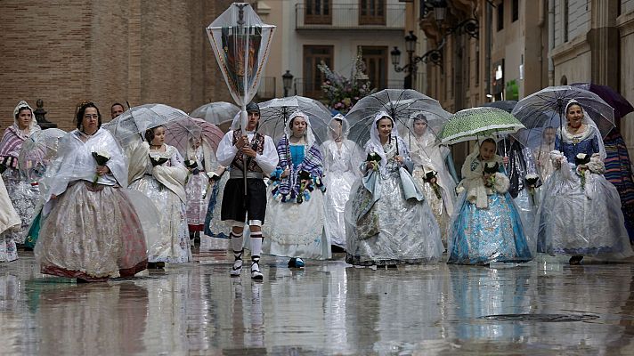 Grupo de personas, mayoritariamente mujeres, con trajes regionales españoles y paraguas, caminan por una calle mojada en una procesión o desfile.
