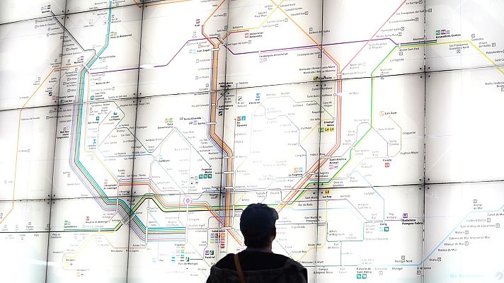 Persona observa mapa iluminado de red de transporte público con líneas de colores y estaciones, en un contexto de reportaje sobre el sistema ferroviario.