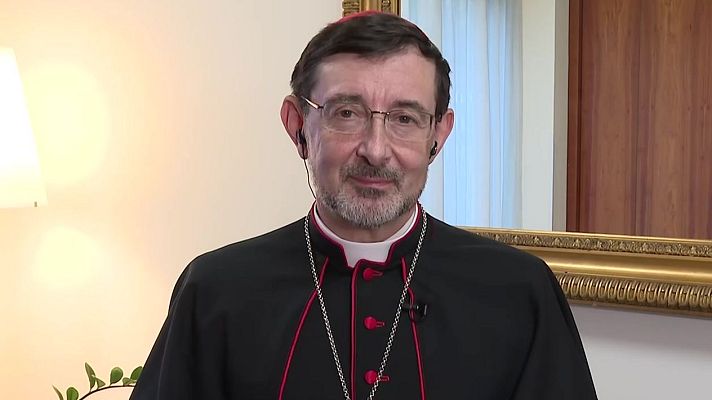 Cardenal con sotana negra y ribetes rojos, gafas y barba, en interior con micrófono, posiblemente durante una entrevista.